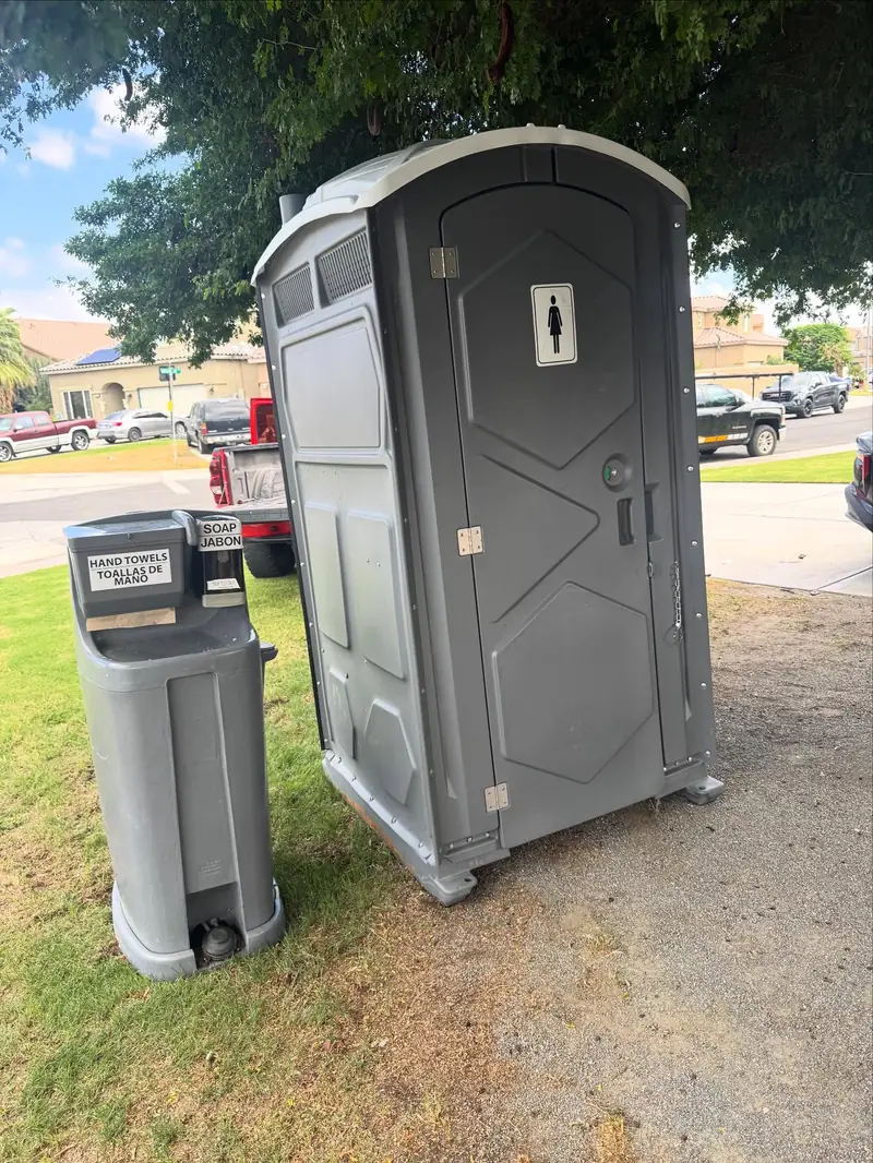 Gray portable toilet next to a handwashing station